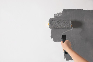 Woman painting white wall with grey dye, closeup. Space for text