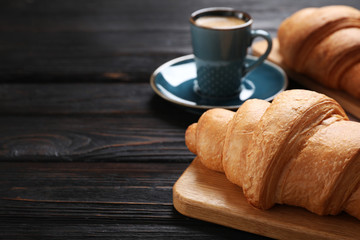 Tasty fresh croissants and coffee on black wooden table, closeup. Space for text