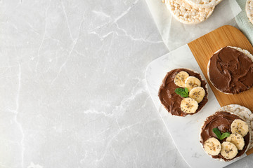 Puffed rice cakes with chocolate spread, banana and mint on grey marble table, flat lay. Space for...