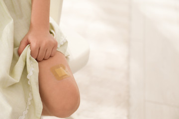 Girl with sticking plaster on leg indoors, closeup