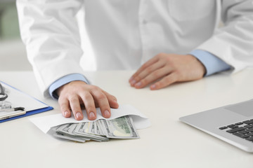 Doctor with bribe at desk in clinic, closeup. Corrupted medicine