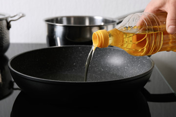 Woman pouring cooking oil from bottle into frying pan, closeup