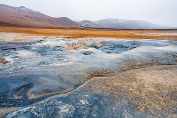 Bubbling geothermal hot/mud pool in the Hverarond area near Myvatn in the Icelandic landscape. Colorful and textured volcanic mineral rich sulphur ground infront.