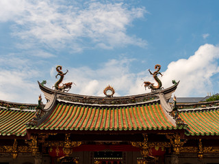 Decorative roof of a Chinese temple in Singapore with two oriental Chinese dragons chasing a flaming pearl against a blue sky, representing power, strength, prosperity and good fortune