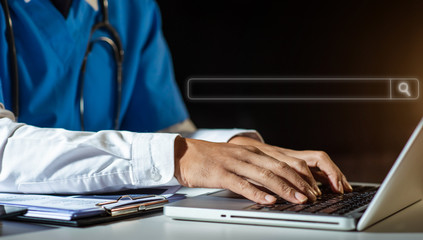 Male doctor hands typing on laptop computer keyboard,searching medical information with textbook on the desk at office. Online medical,medic tech, emr, ehr concept.