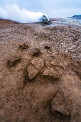 Hot sulfuric steam vent spewing sulphur steam in the hot sulfuric and geothermal area of Namaskard in Myvatn/Iceland. Color and mineral rich textured muddy ground infront.