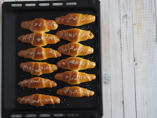 Ready-made toasted homemade bagels on a black baking sheet from the oven. Ready to eat. Sprinkled with sesame seeds. Home kitchen.