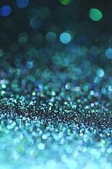 Blue glitter with green bokeh on a black background. Turquoise glitter brilliant mockup.  background with twinkle lights.blue shiny  glitter layout.