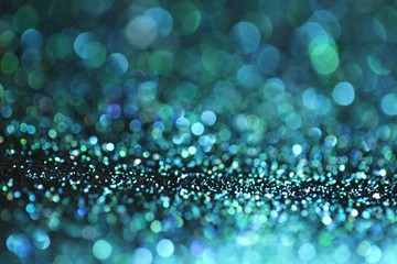 Blue glitter with green bokeh on a black background. Turquoise glitter brilliant mockup.Vibrant...