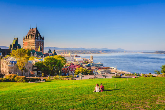 Cityscape view of Old Quebec City with buildings, green grass against St Lawrence river and blue sky in summer evening