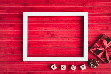 Happy Valentines Day with Empty white Photo Frame, LOVE Cube Boxes, Gift, Pine Cone on Red Wooden Table in Backgroundd