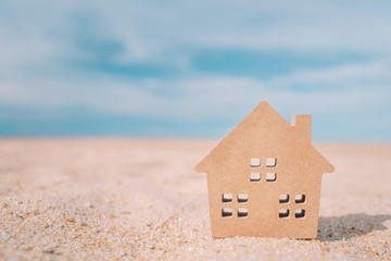 Fototapeta na wymiar Small home model on sunset beach sand texture background.