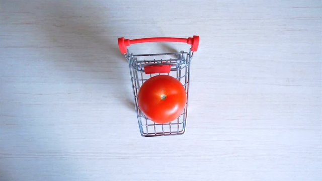 Small shopping trolley and tomato.  Female hand moves small trolley with tomato to the centre of table. Buying healthy food.