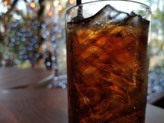 Close up sparkling cola in glass with ice on brown wooden barrels light bokeh background.