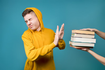 A girl holds out a stack of books to a young guy in a yellow sweatshirt on a blue background, and...