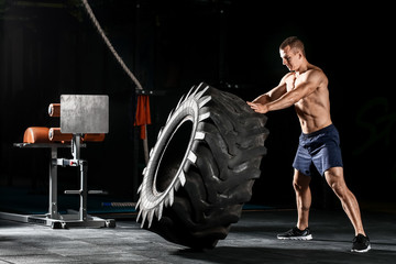 Fototapeta na wymiar Sporty muscular man flipping a heavy tire in gym