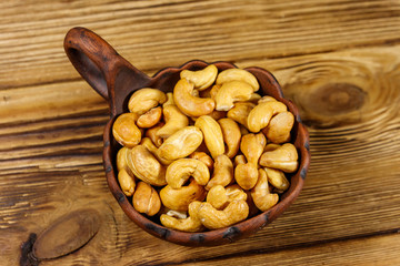 Ceramic bowl with roasted cashew nuts on a wooden table. Top view