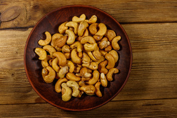 Ceramic plate with roasted cashew nuts on a wooden table. Top view