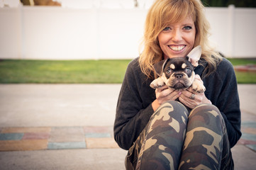 Pretty blonde woman happily holding a funny black and tan French bulldog puppy