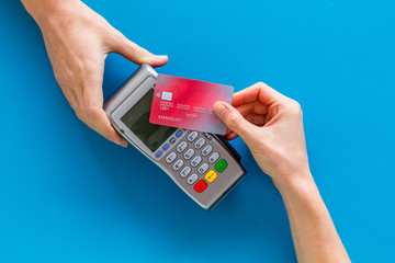 Contactless payment, paypass. Hand hold bank card near terminal on blue background top-down