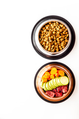 Healthy feed for cats and dogs. Bowls full of dry feed, meat and vegetables on white background top-down copy space