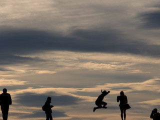 silhouette of people, one jumping,  against a evening cloudscape with space for copy