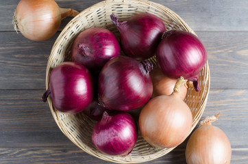 Red onions in a wicker basket. Brown wooden background.