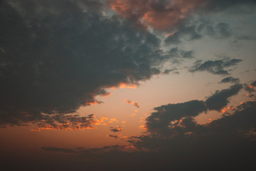 Cloudy dramatic sky at sunset with orange clouds and sunlight.