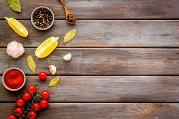 Cooking background with spices - pepper, garlic, cherry tomatoes - on dark wooden desk top-down frame copy space