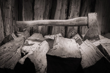 Hatchet axe being stuck in a pile of split wood logs used for fire. Concept of making logs with natural colors- Axe viewed from the front and side.