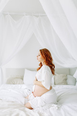 Waiting for a happy baby. Pregnant girl on a white bed.