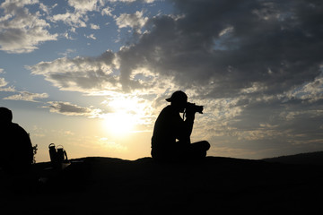 Photographer man silhouette, sitting & taking pictures with a DSLR Camera