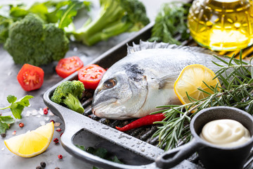 One raw dorado fish with spices, lemon and parsley in a black grill pan on a white concrete background. Healthy eating and tasty culinary concept. macro