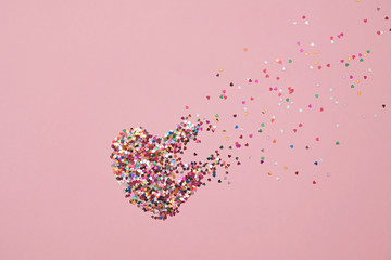 Valentine day composition with broken heart made from confetti on pink background