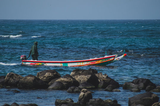 Typical fishing boat in Almadies, Dakar, Senegal, called pirogue or piragua or piraga with a fisherman driving the boat into a bay on a clear sunny day.