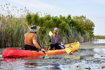Couple (man and a woman) kayaking on a wild river among reeds and lilies