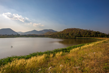 The blurred panoramic nature background of sunlight hitting the lake's surface, grass and wind blowing all the time along the large mountains, ecological beauty and fresh air.