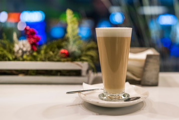 Latte coffee in a tall glass, against the window. Photographed close-up.