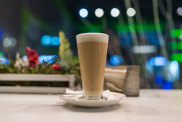 Latte coffee in a tall glass, against the window. Photographed close-up.