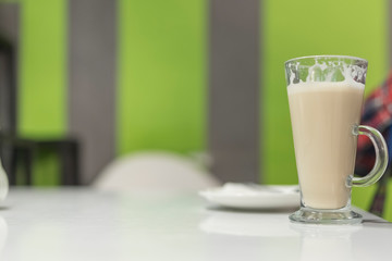 Latte coffee in a tall glass, against the window. Photographed close-up.