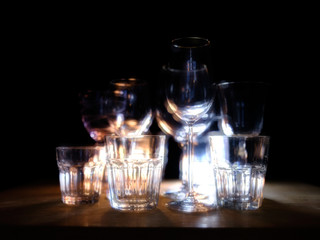 Close ups of wine-, long drink- and spirits-glasses on a wooden shelve in a bar, in front of a dark background, illuminated by colorful spot lights, creating blurry light effects with beautiful  bokeh