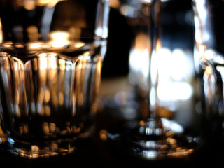 Fototapeta na wymiar Close ups of wine-, long drink- and spirits-glasses on a wooden shelve in a bar, in front of a dark background, illuminated by colorful spot lights, creating blurry light effects with beautiful bokeh