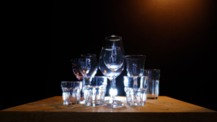 Close ups of wine-, long drink- and spirits-glasses on a wooden shelve in a bar, in front of a dark background, illuminated by colorful spot lights, creating blurry light effects with beautiful  bokeh