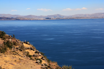 A Knitting Man sitting on the Edge of the Cliffs on Taquile Island overlooking Lake Titicaca towards Bolivia