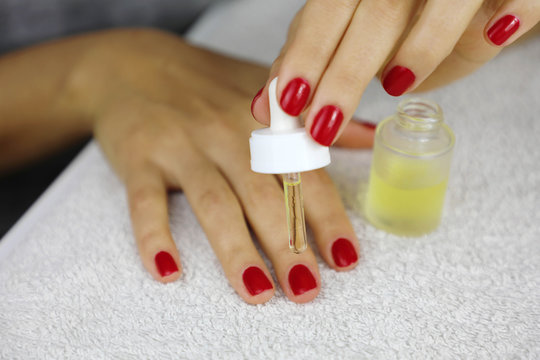 Manicure oil hand. Female hands take care of cuticles with oil. Girl with red nail polish sitting at the table and takes care of her cuticles.