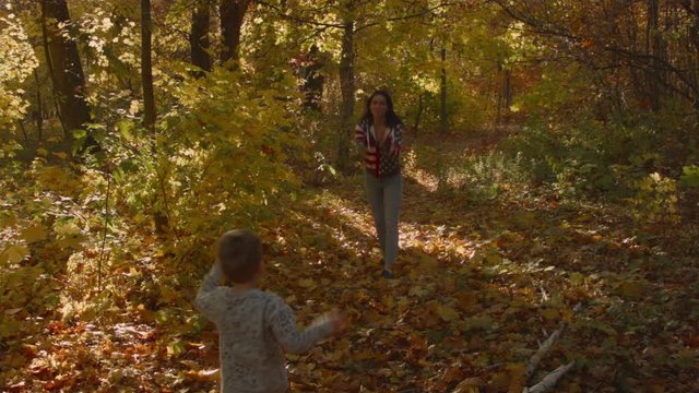Young Caucasian woman with a child playing a ball in the autumn forest. Recorded in Raw on Blackmagic camera.