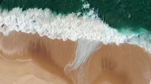 Aerial view of drone flying above beautiful beach with views of ocean waves and water crashing on to sandy beach from top angle