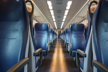 blue lined seats lined up along the corridor of a regional train with no passengers during the day