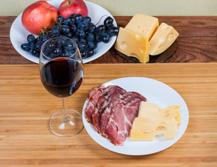 Red wine against cheese, cured pork slices and fresh fruits