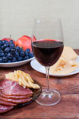 Red wine against the cheese, cured pork, fruits close-up